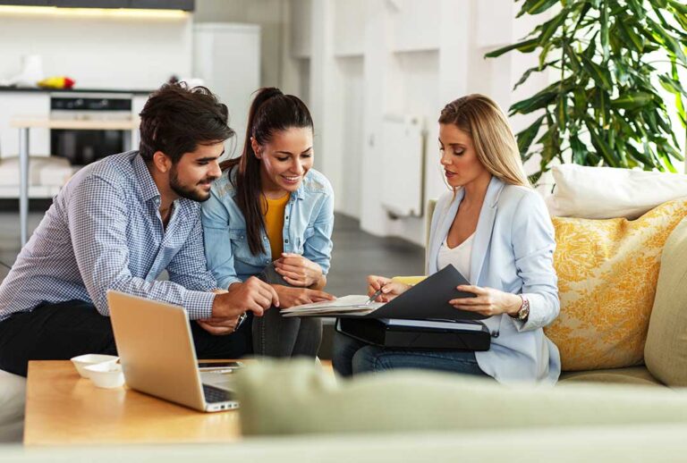 A family sorting through home insurance documents at a dining table surrounded by renovation plans and personal belongings.